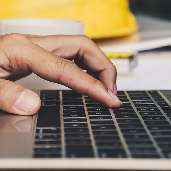 A person working on a laptop computer with a hard hat in the background.
