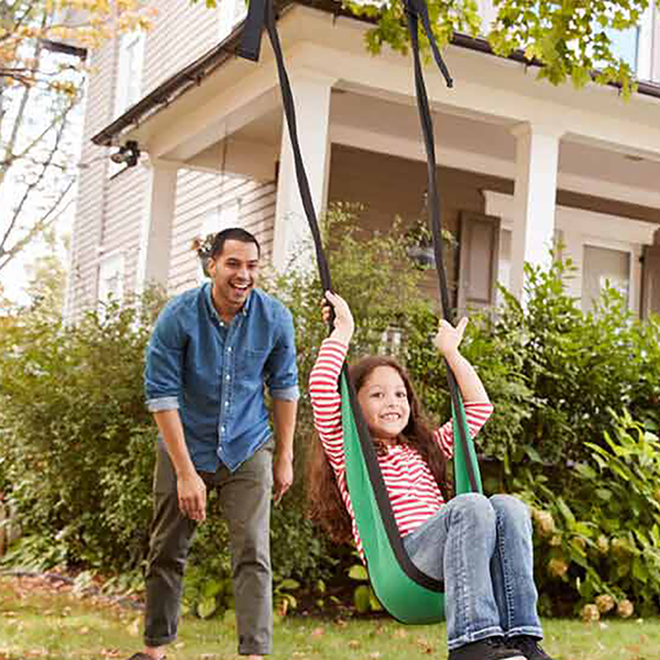 A father and child playing on a swing in their front yard.
