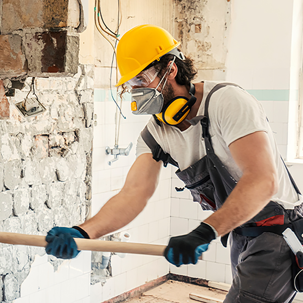 A contractor demolishing a brick wall with a hammer.