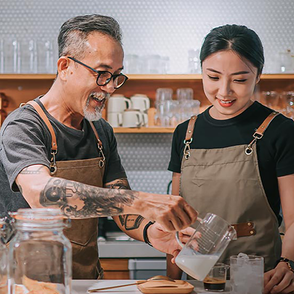 A small business owner teaching an employee how to pour coffee in a cafe.