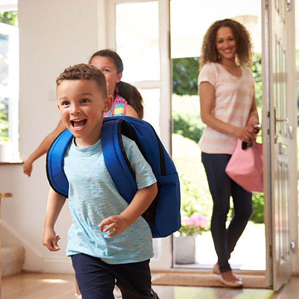 Two children and their mom coming home. The children are wearing backpacks.