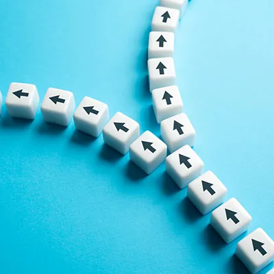 A line of white cubes with black arrows printed on them splitting into two branches.