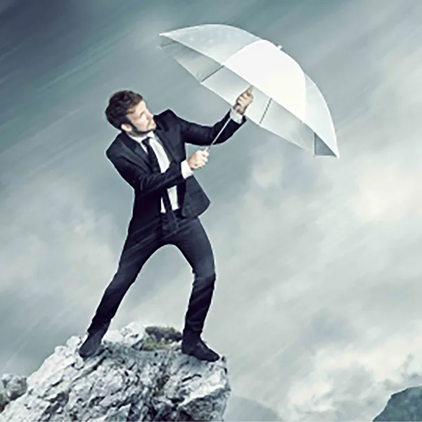 A man wearing a suit holding an umbrella against wind and rain.
