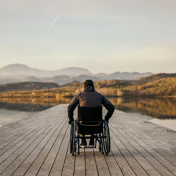 A wheelchair user sitting on a dock looking out at a lake.