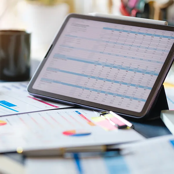 A tablet computer showing a spreadsheet propped up on a desk.