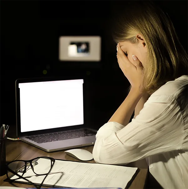 A woman looking with frustration at a laptop computer in a dark room.