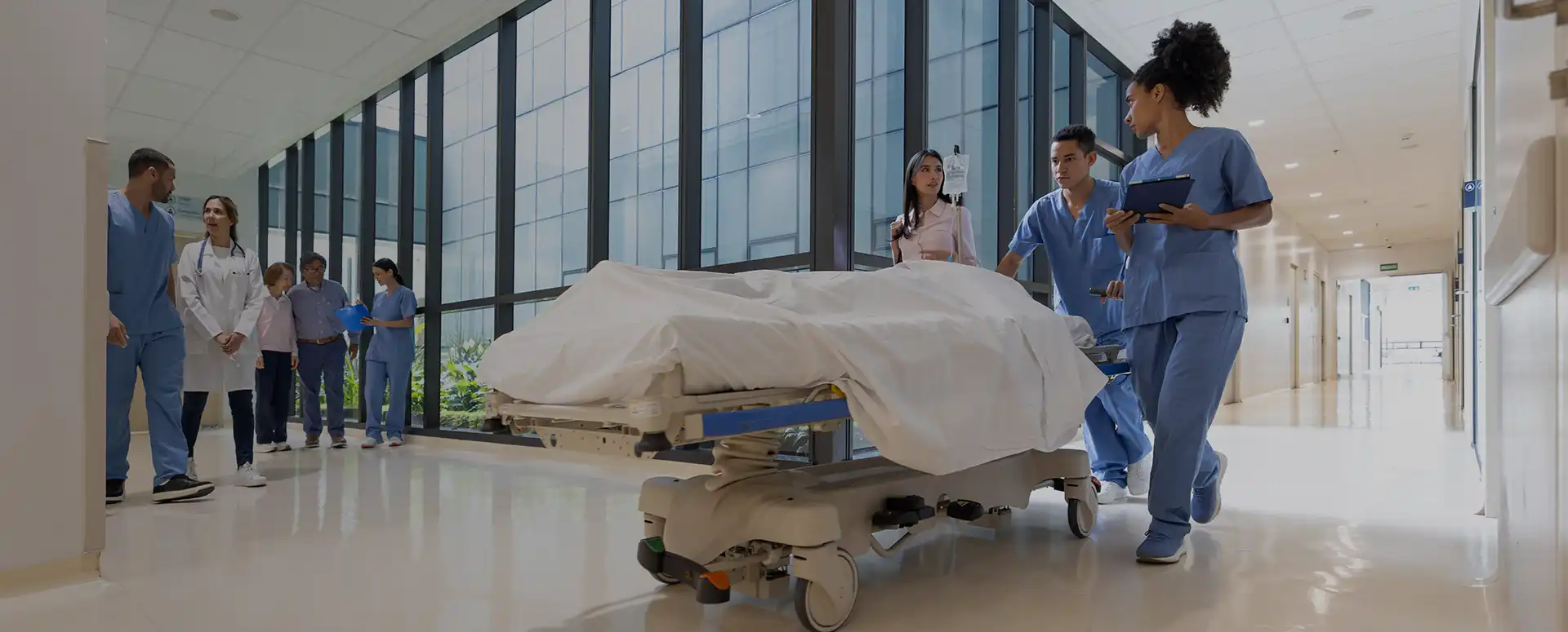 A medical team walks with a gurney carrying a patient down a hospital hallway.