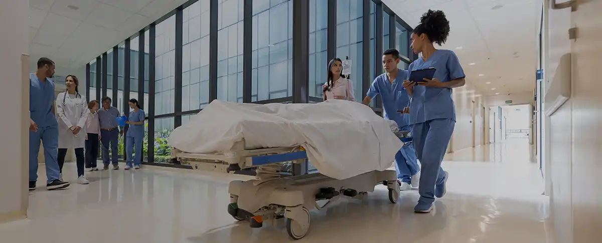 A medical team walks with a gurney carrying a patient down a hospital hallway.