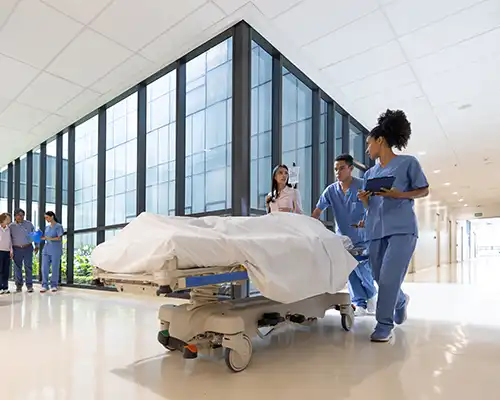 A medical team walks with a gurney carrying a patient down a hospital hallway.