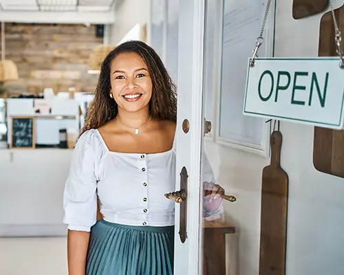 A smiling woman stand in the open doorway of her small business.