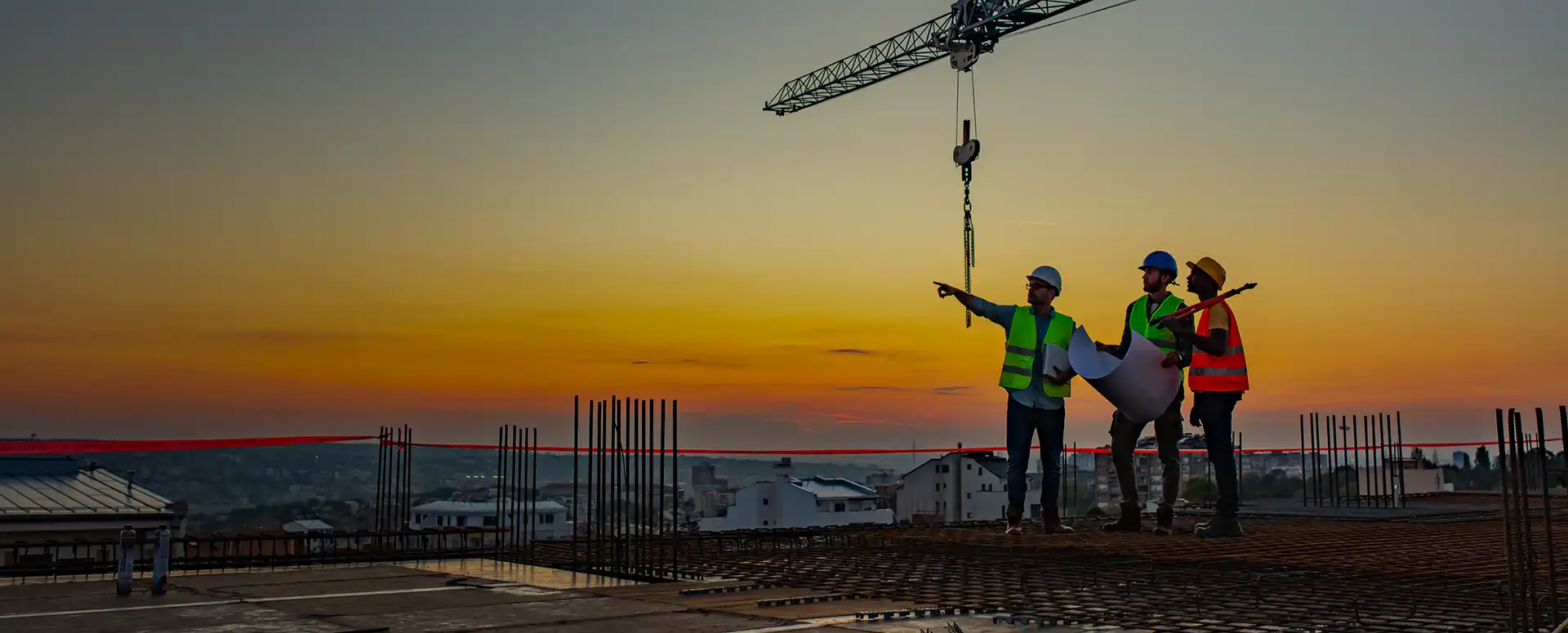 Three contractors in safety vests and hard hats on the top of a job site.