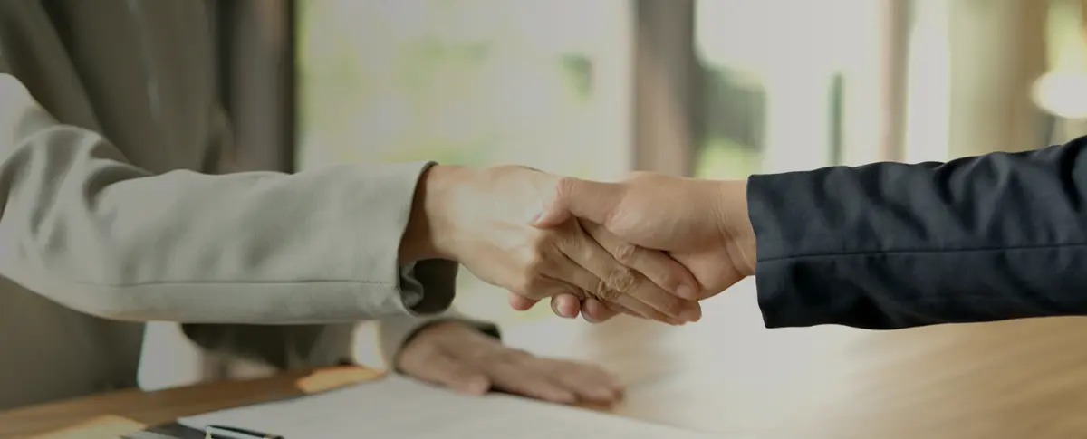 Hand clasped in a handshake over documents lying on a table. 