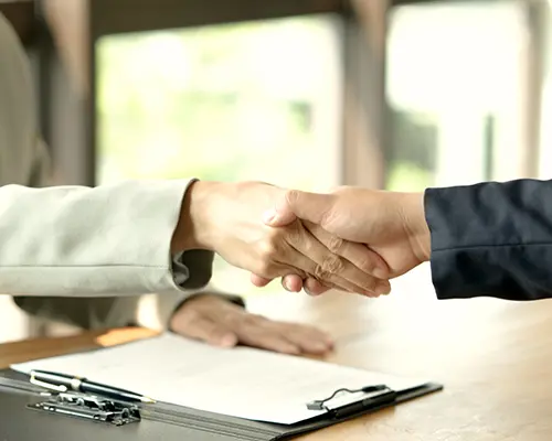 Hand clasped in a handshake over documents lying on a table. 