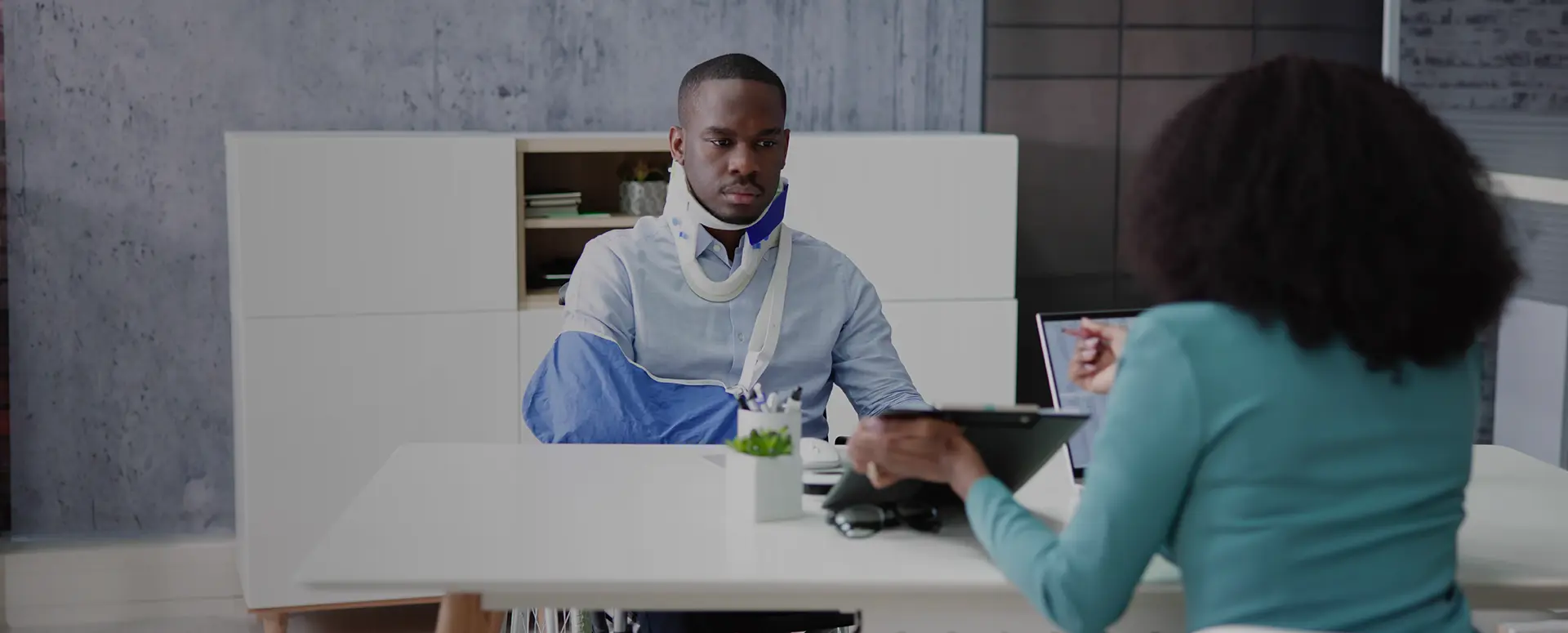 A construction worker wearing a safety vest and hard hat carries a metal beam on his shoulder.