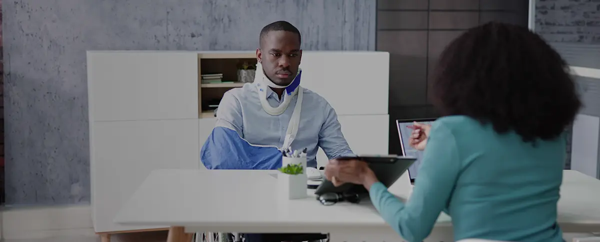 A construction worker wearing a safety vest and hard hat carries a metal beam on his shoulder.