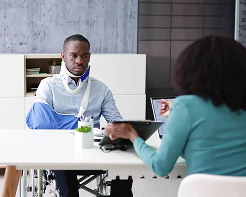 A construction worker wearing a safety vest and hard hat carries a metal beam on his shoulder.