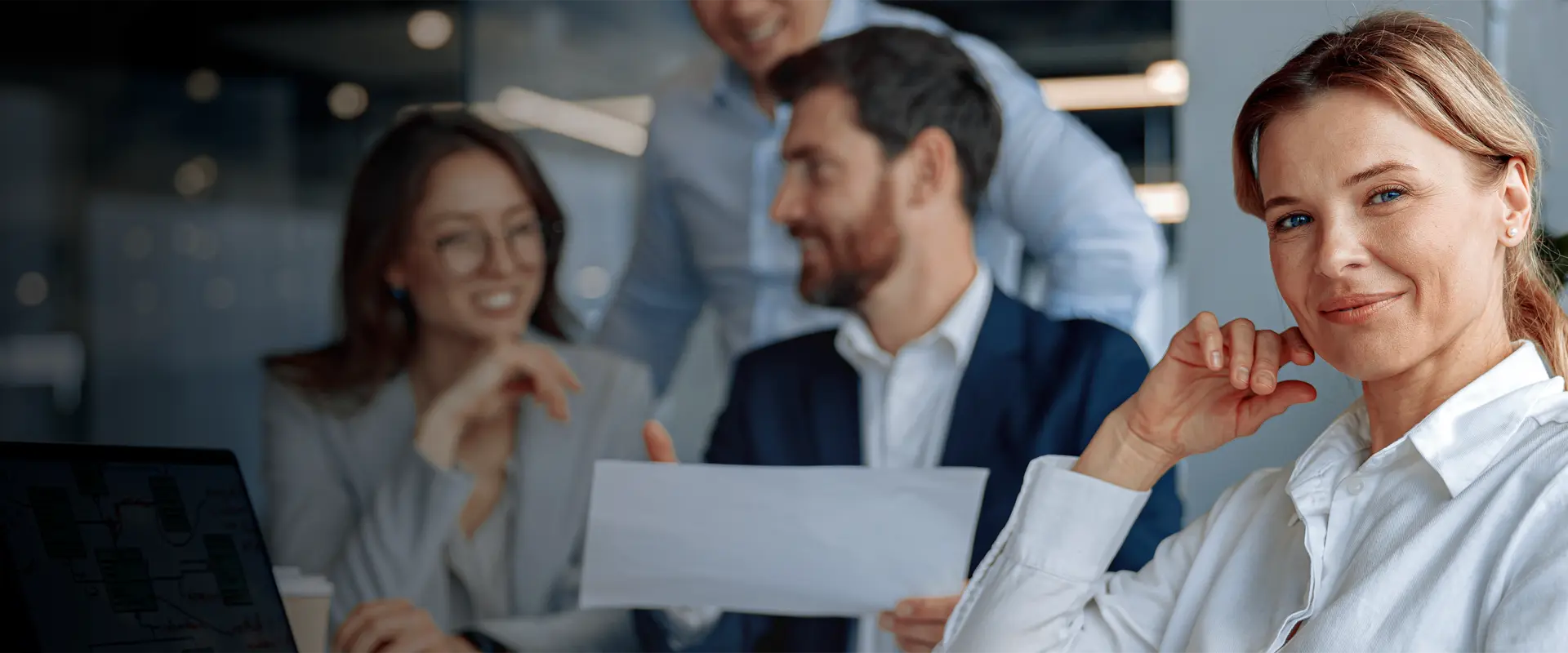 A business woman sitting with a group and and looking at the viewer.