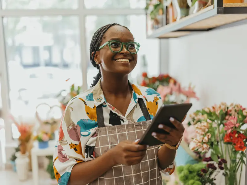 A smiling woman standing in a flower shop holding a clipboard.