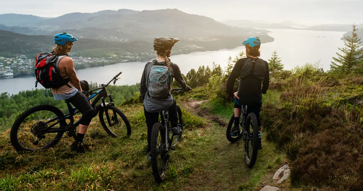 A group of mountain bikers on a hilltop overlooking a lake and mountains.