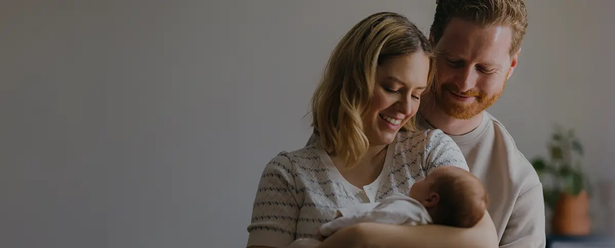 A man & woman smiling at a baby being held in the woman's arms.
