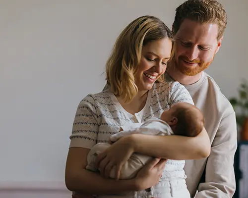 A man & woman smiling at a baby being held in the woman's arms.