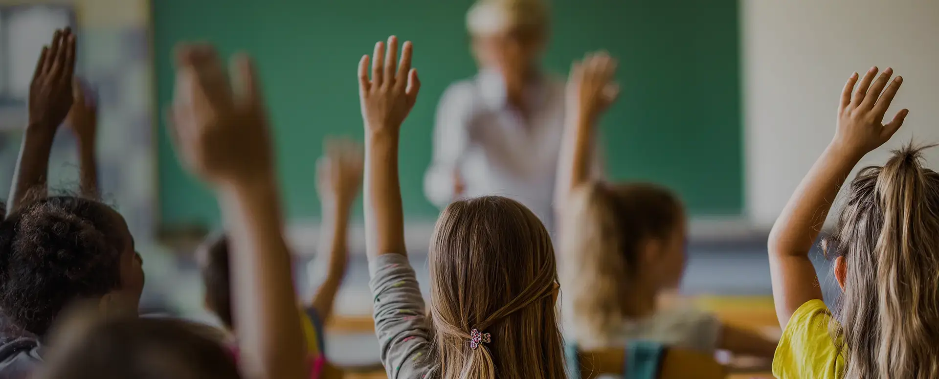 A group of students raising their hands in a classroom.