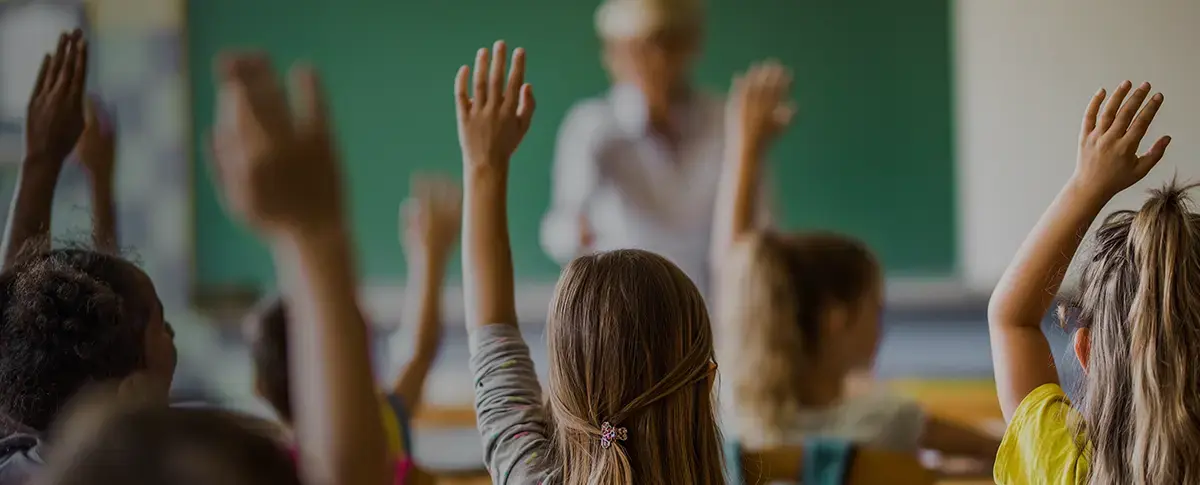A group of students raising their hands in a classroom.