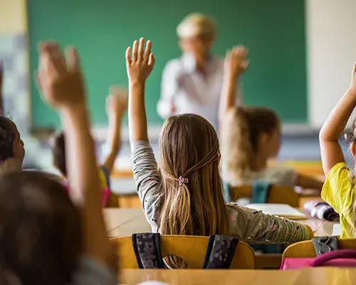 A group of students raising their hands in a classroom.
