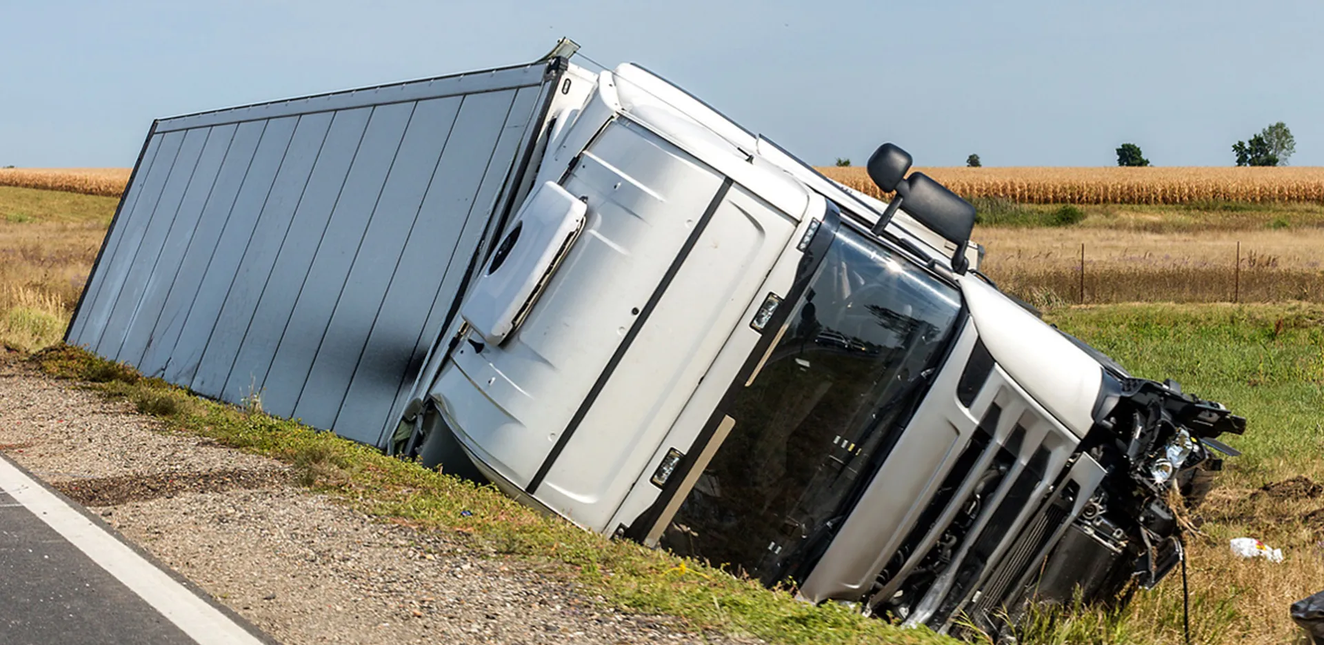 A crashed semi truck laying on it's side on the edge of a highway.