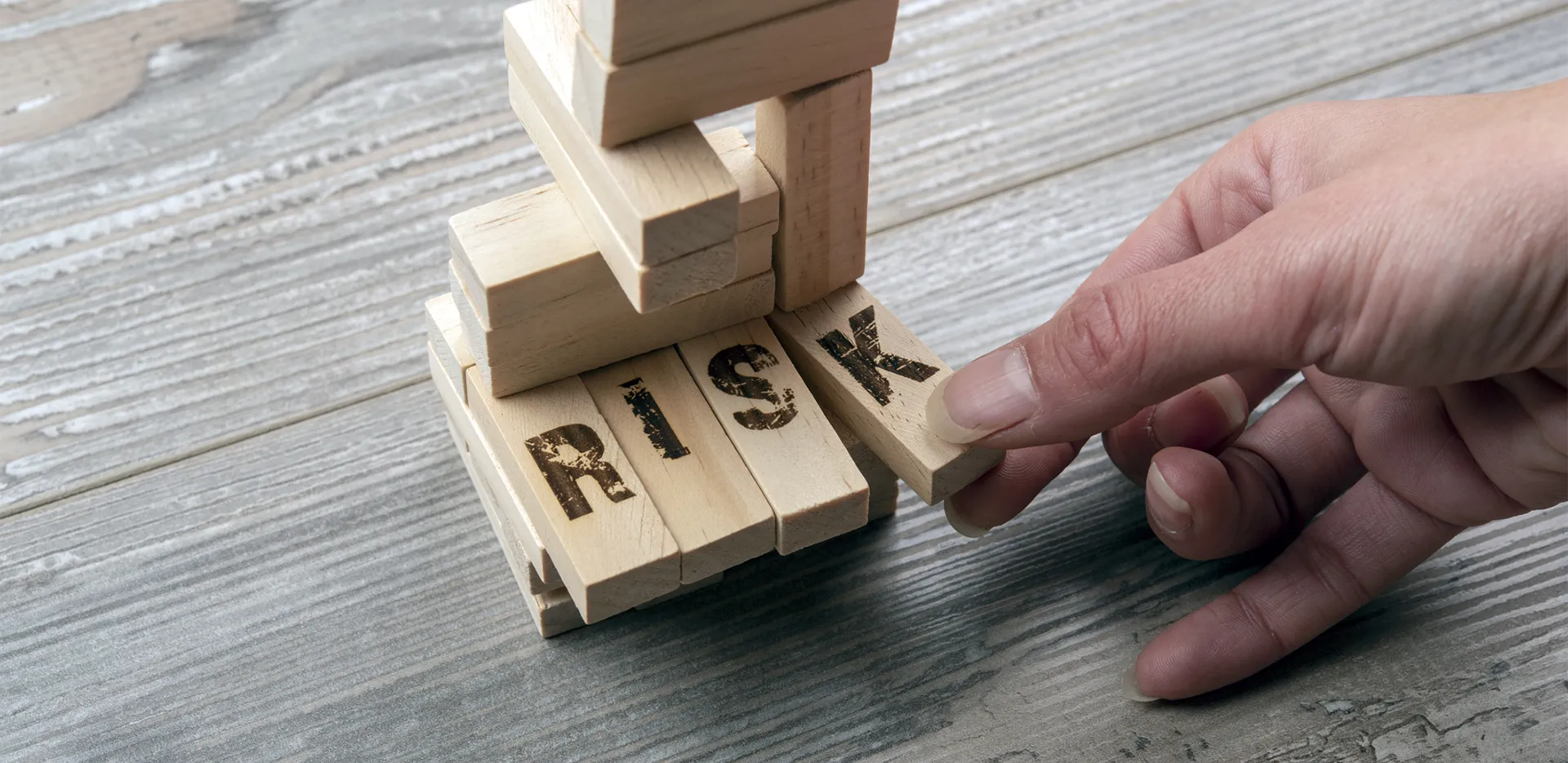 Someone about to knock over a tower of Jenga blocks. The blocks have 'RISK' written on them.