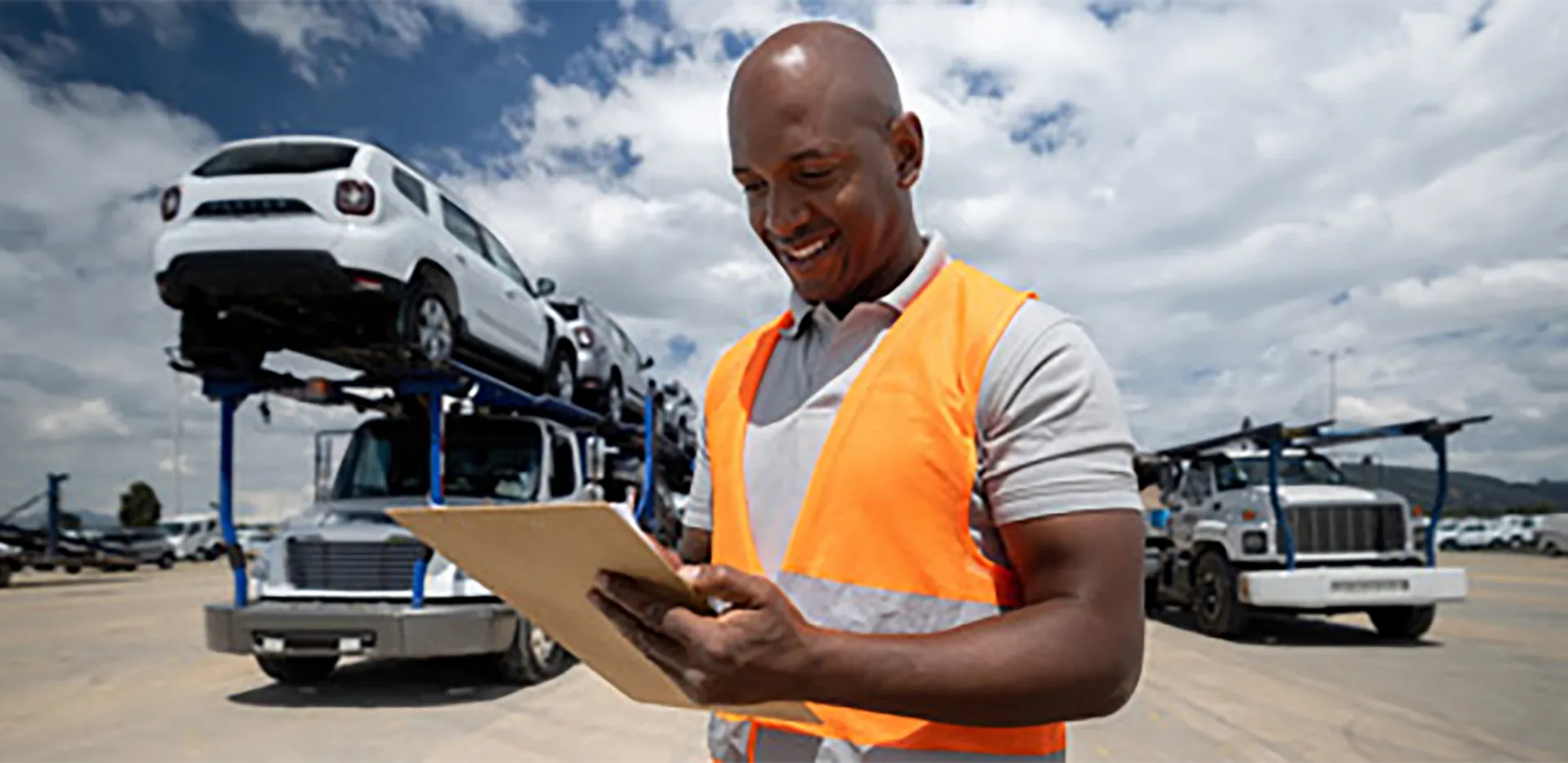 A professional wearing an orange vest with a vehicle transport truck in the background.