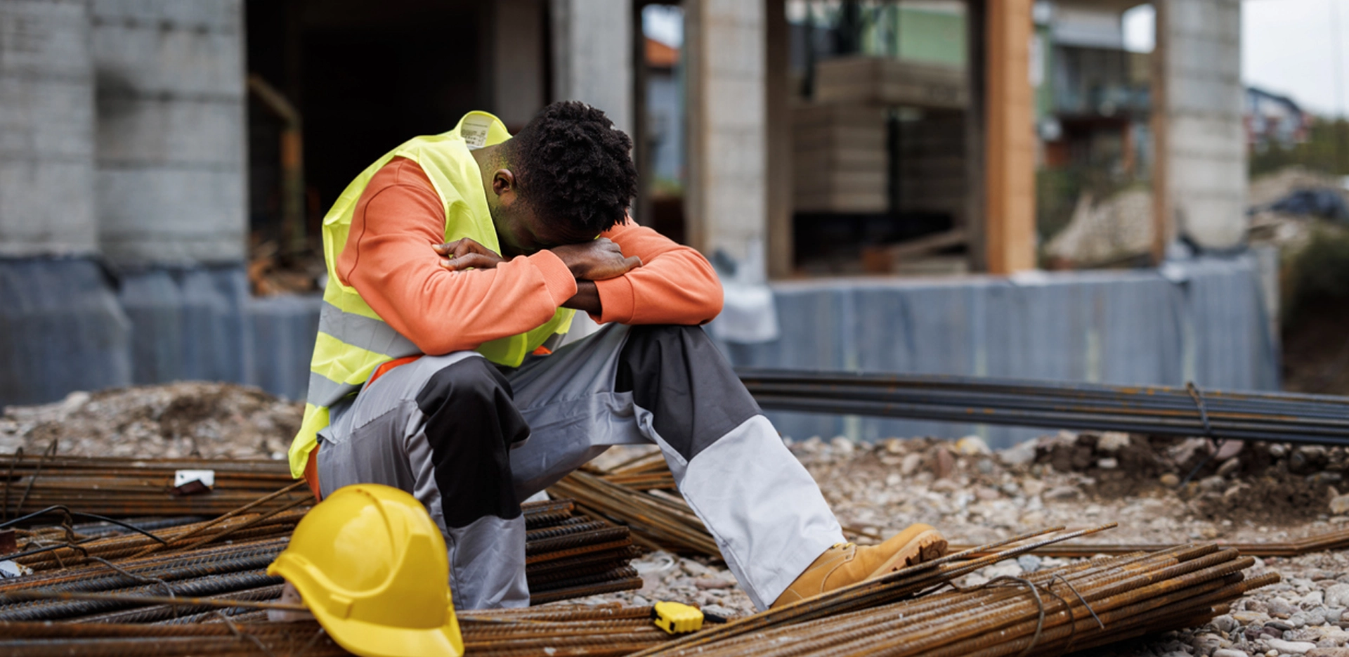 exhausted construction worker sitting outdoors, with health resting on his crossed arms