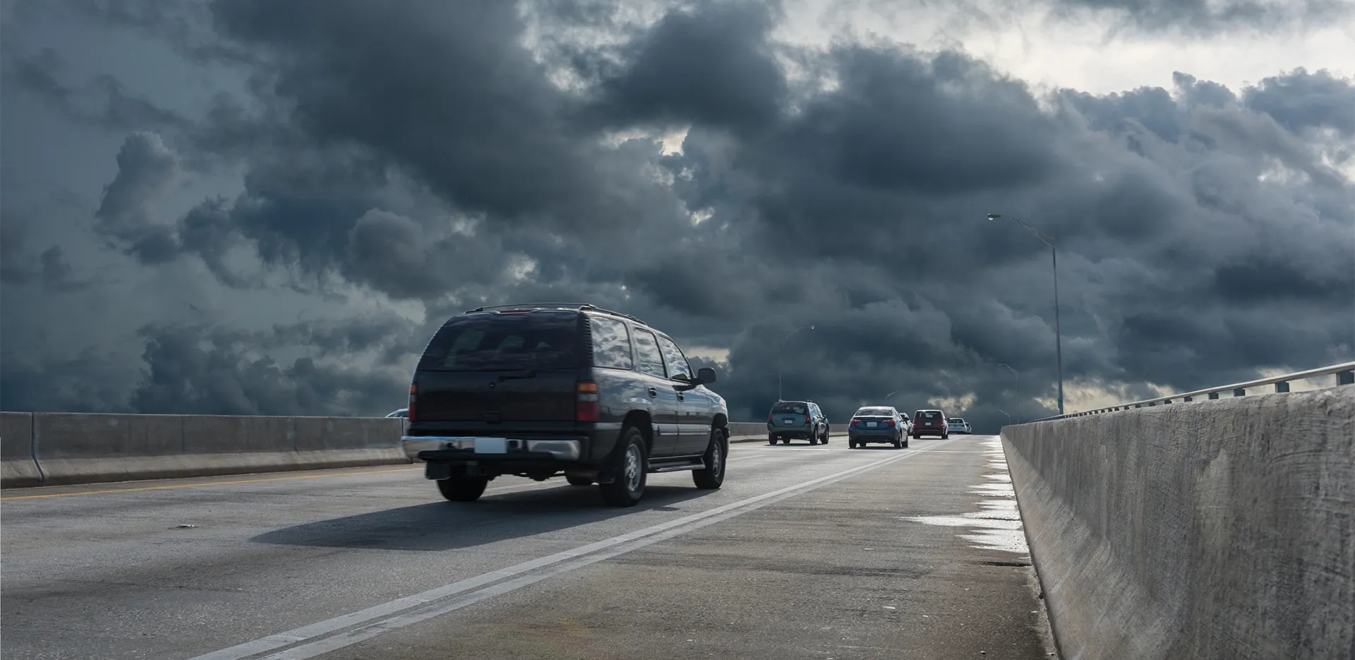 Cars on the highway with dark storm clouds in the background.