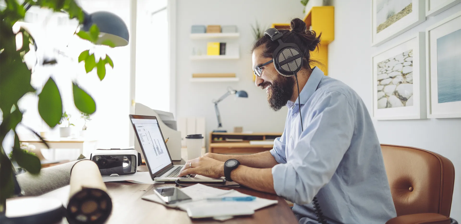 A man working from home at his laptop wearing over-ear headphones.