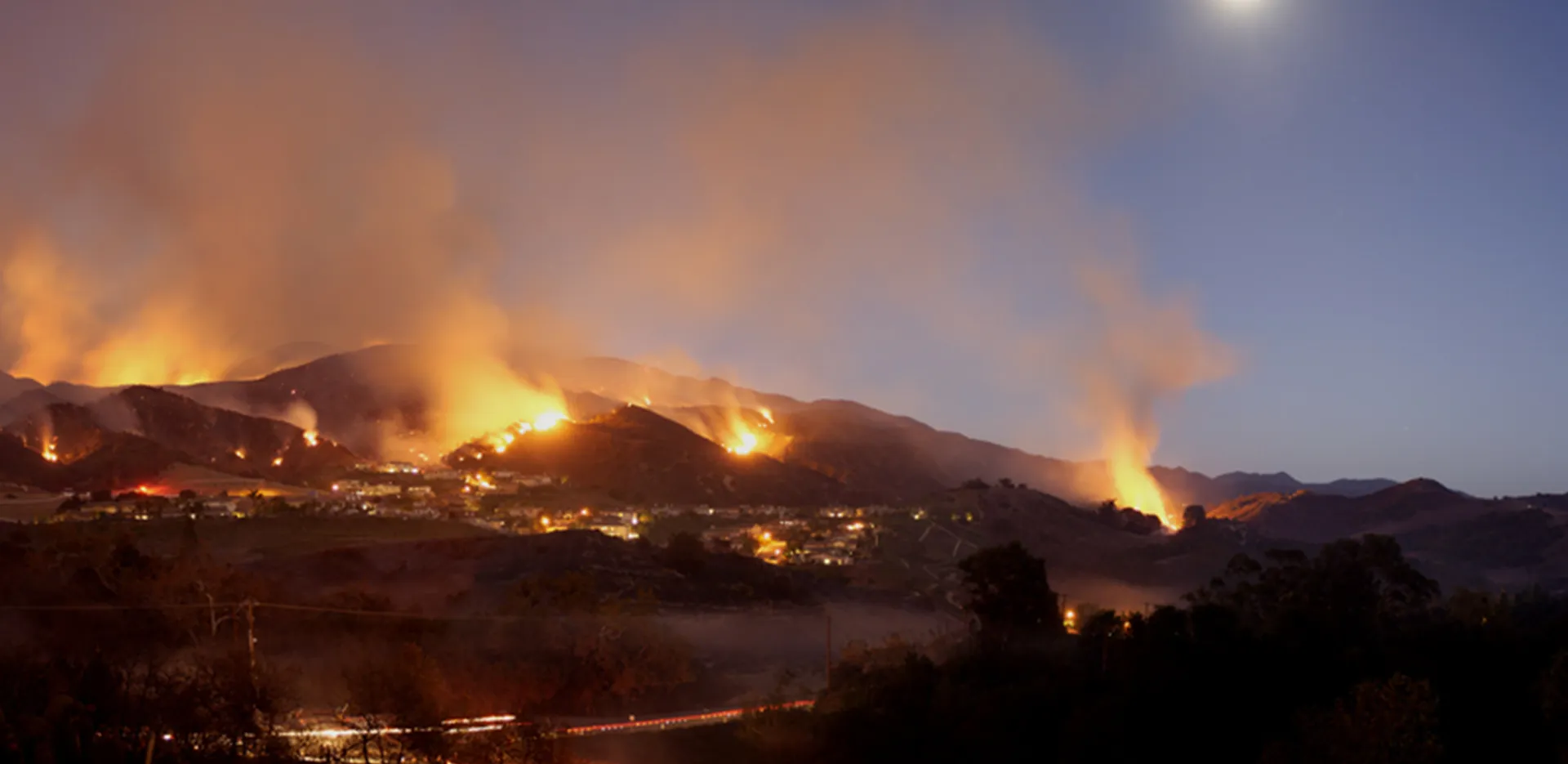 An urban hillside covered in wildfires and smoke.
