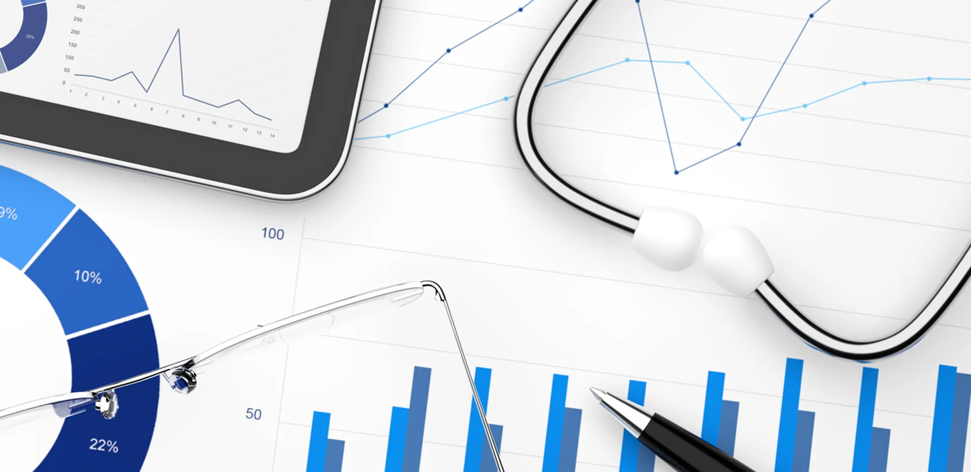 A pen, glasses, tablet, and stethoscope sitting across a background of charts and graphs.