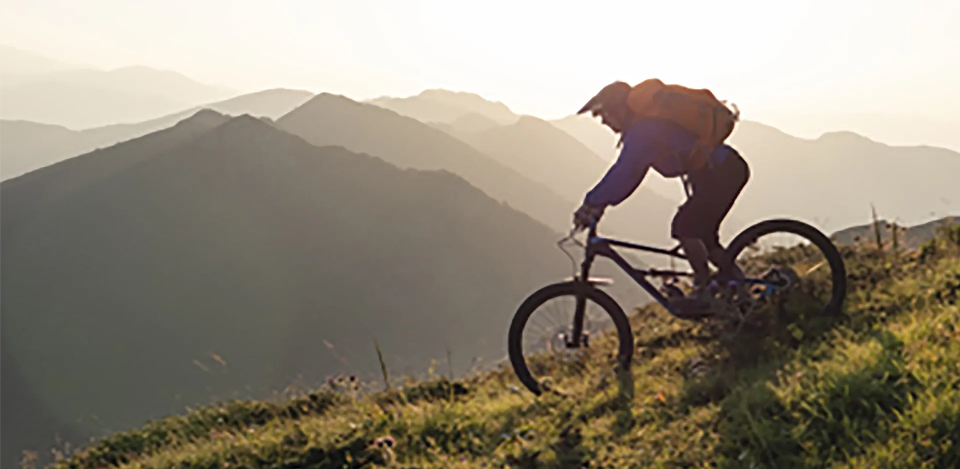 A person cycling down a grassy mountain.