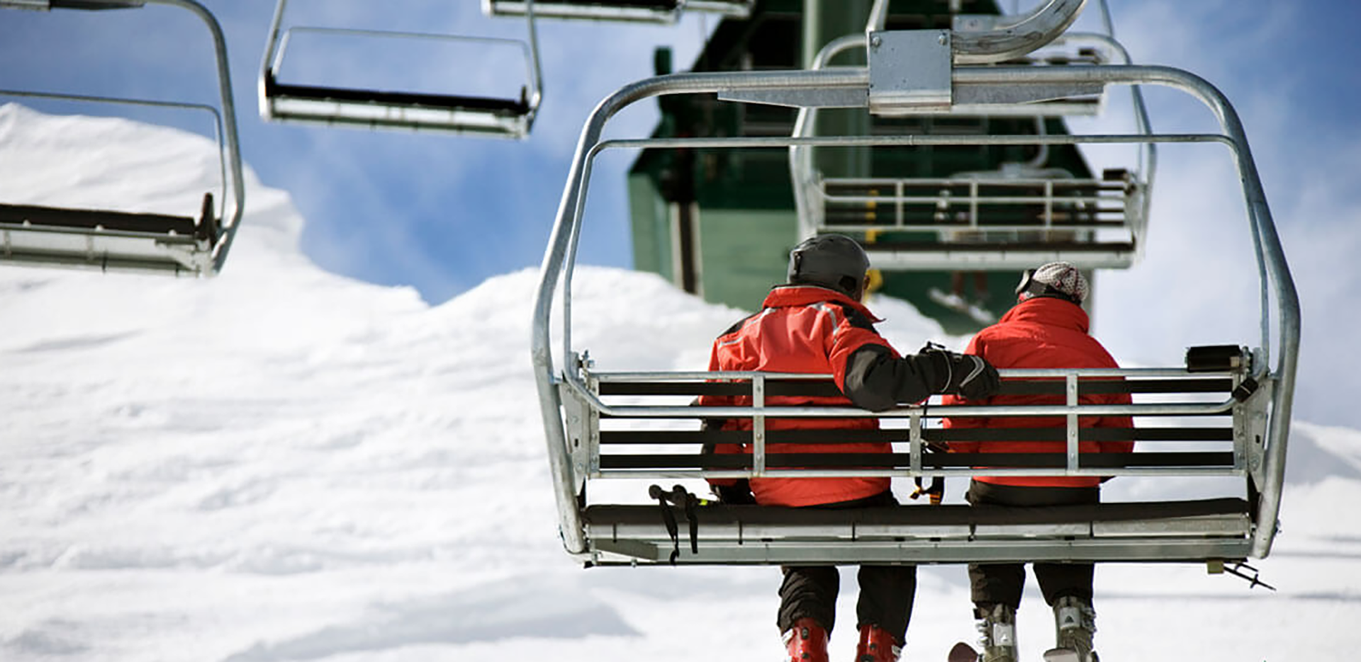 A pair of skiers wearing red jackets riding on a ski lift.