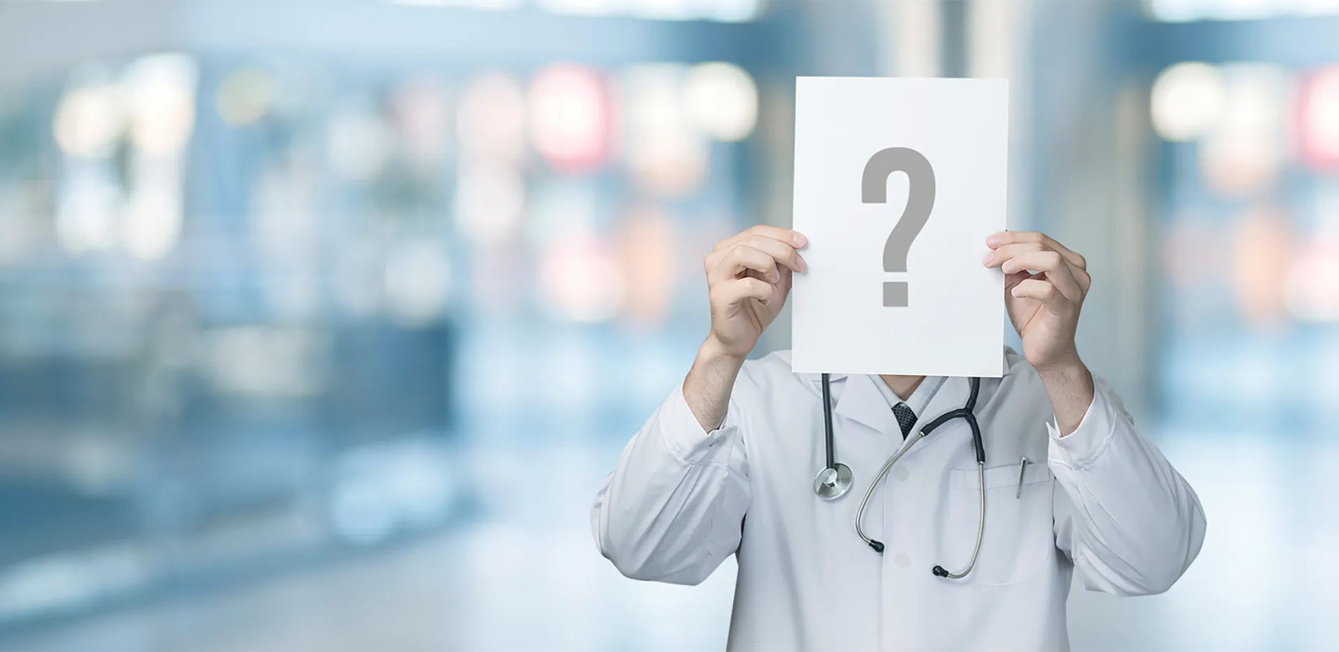 A medical professional holding a piece of paper with a question mark on it in front of their face.