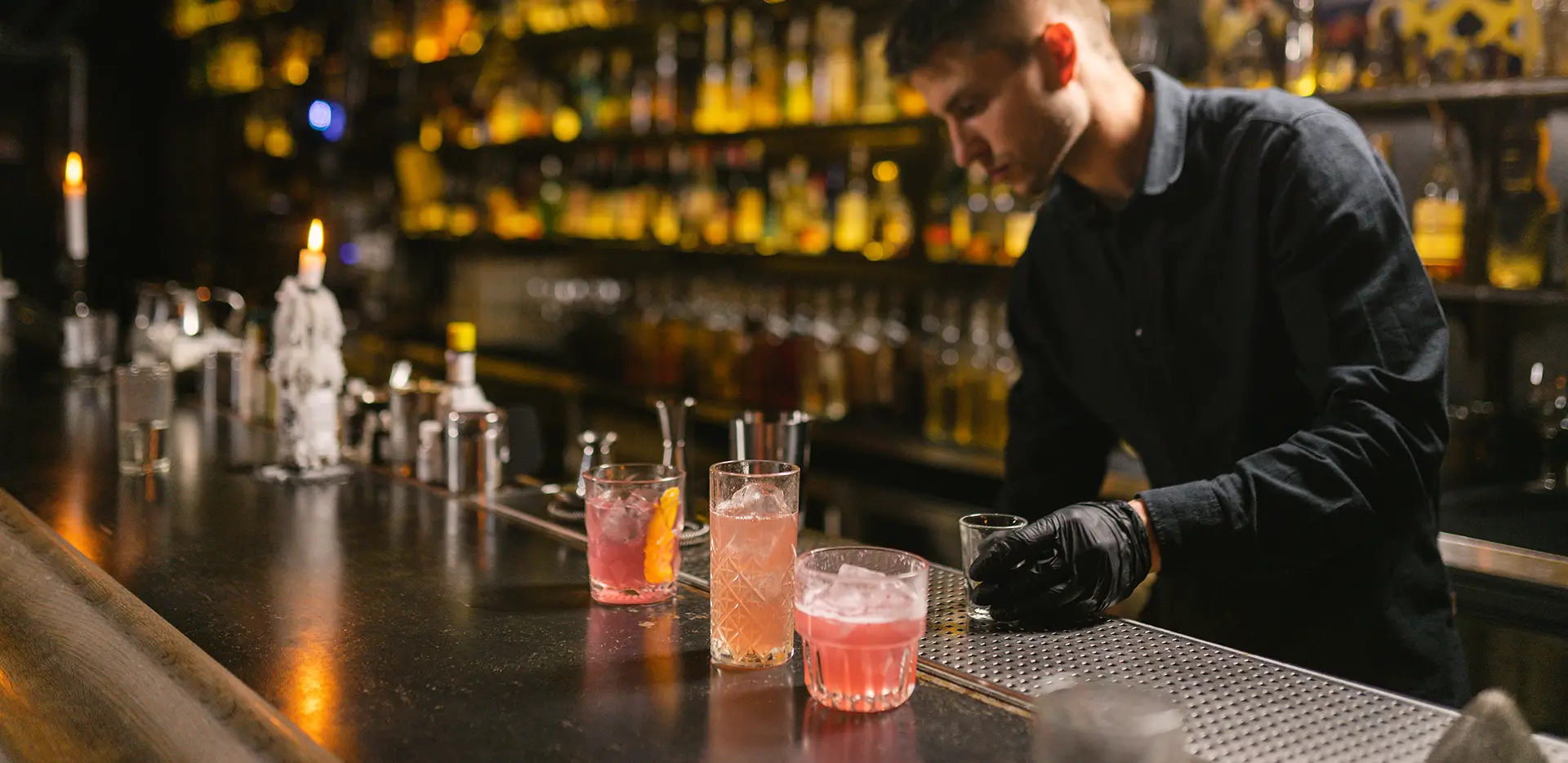 A bartender wearing gloves prepares three cocktails.