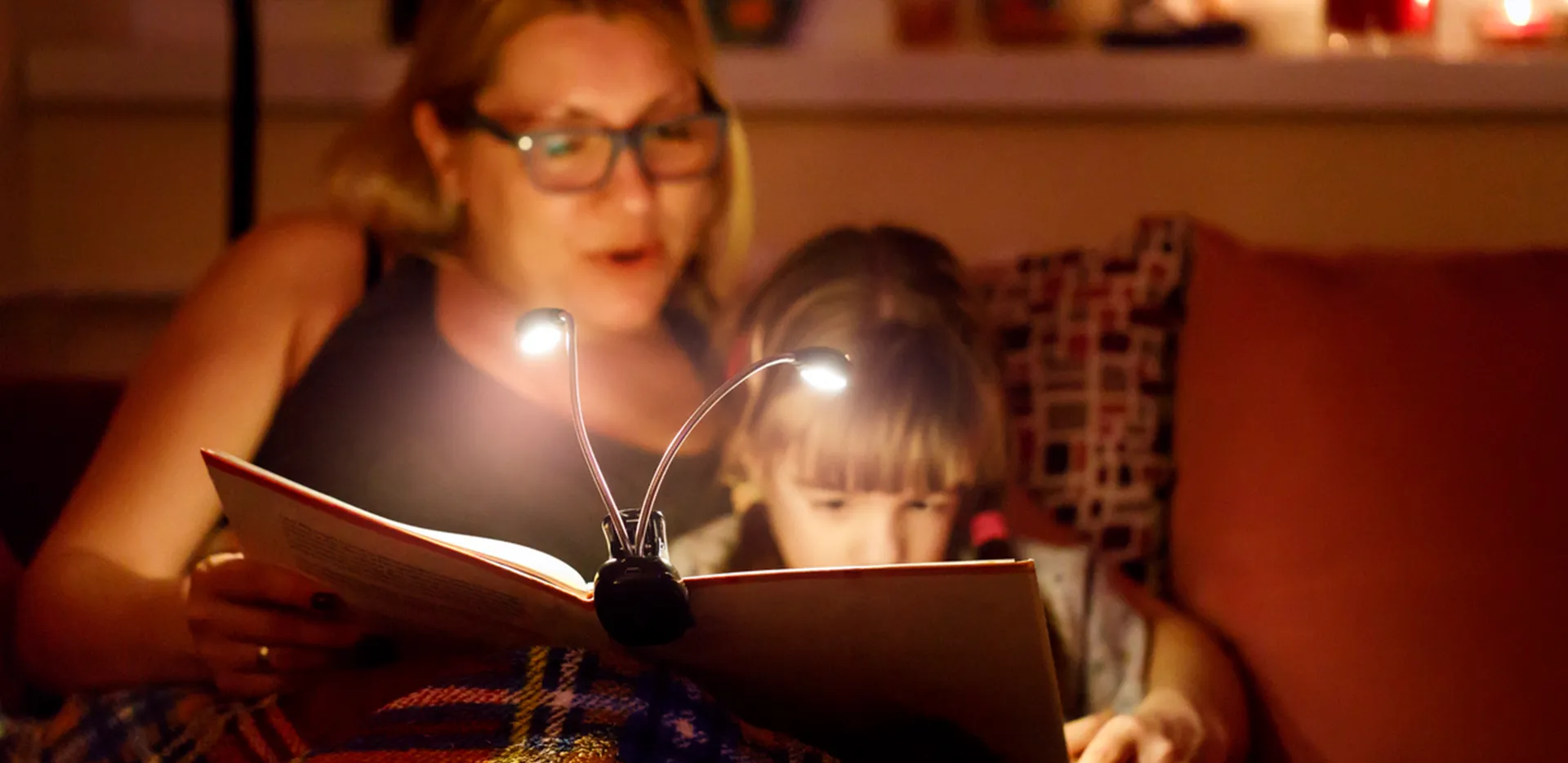 A mother reading a book to her child with the aid of electric book lights.