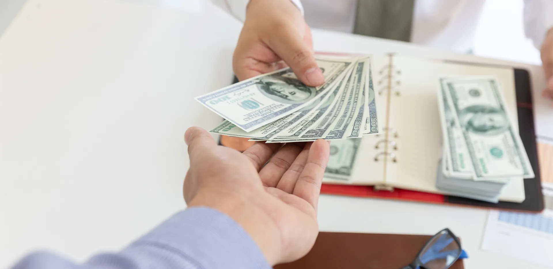 A person handing another person a stack of $100 bills.