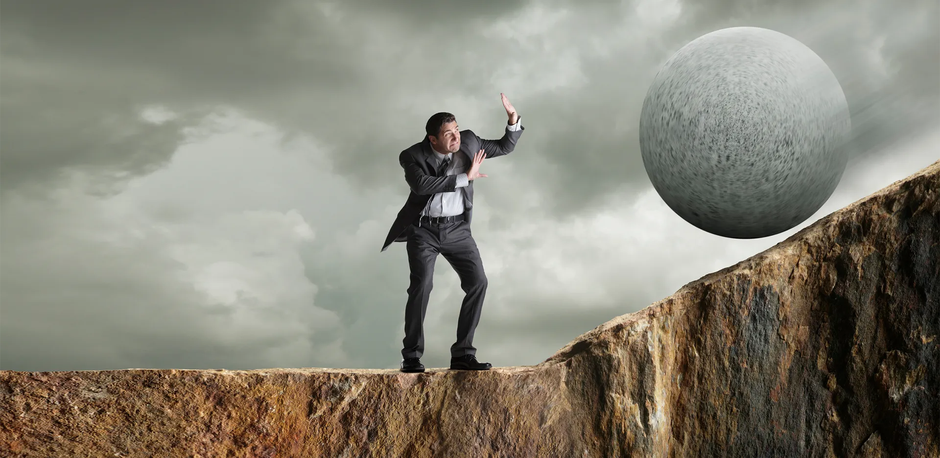 A man wearing a suit holding up his hands as a large boulder rolls towards him.