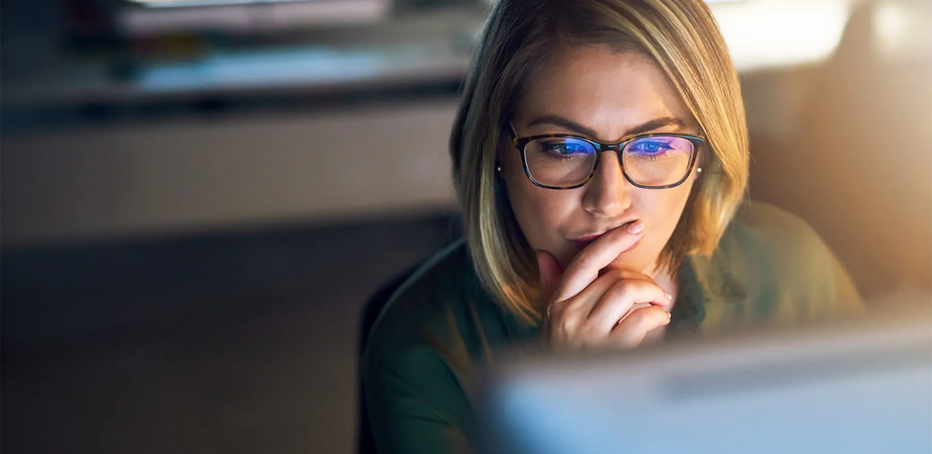 A woman looking pensively at her computer screen.