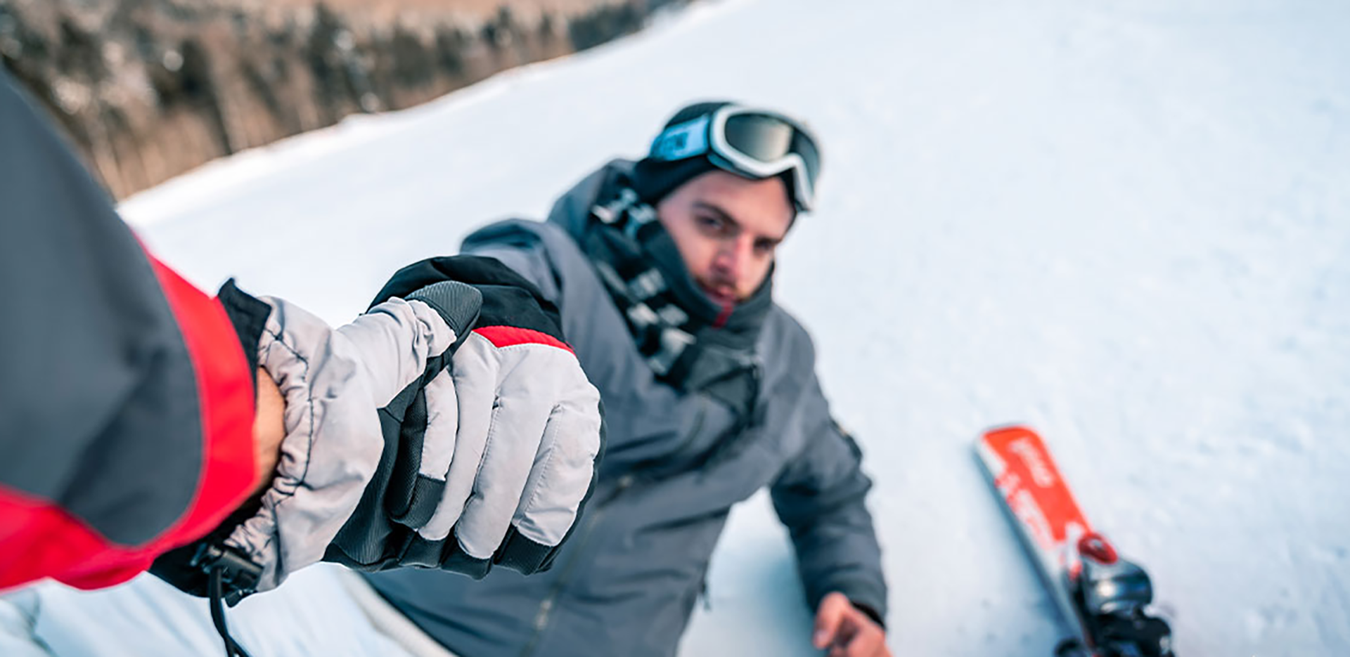 A person helps up a fallen snowboarder.