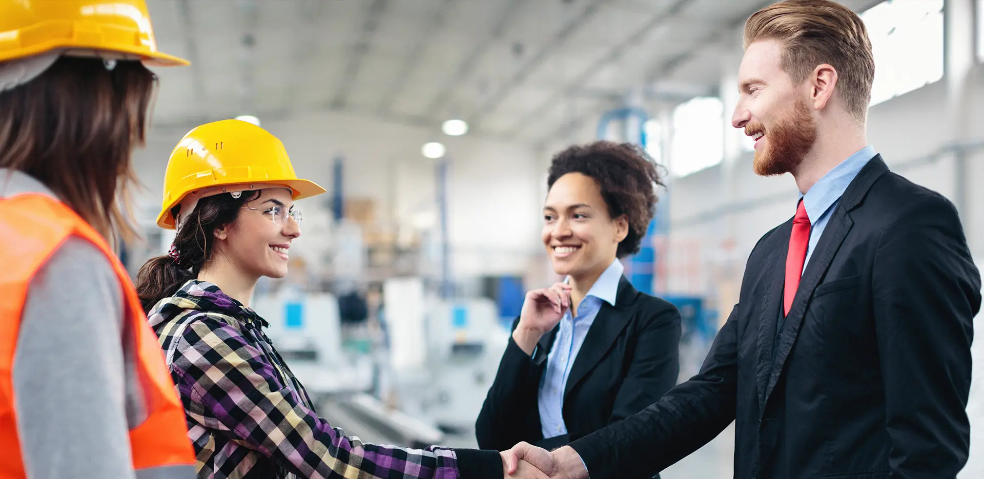 A man in a suit shaking hands with a woman wearing a hard had and tool belt.
