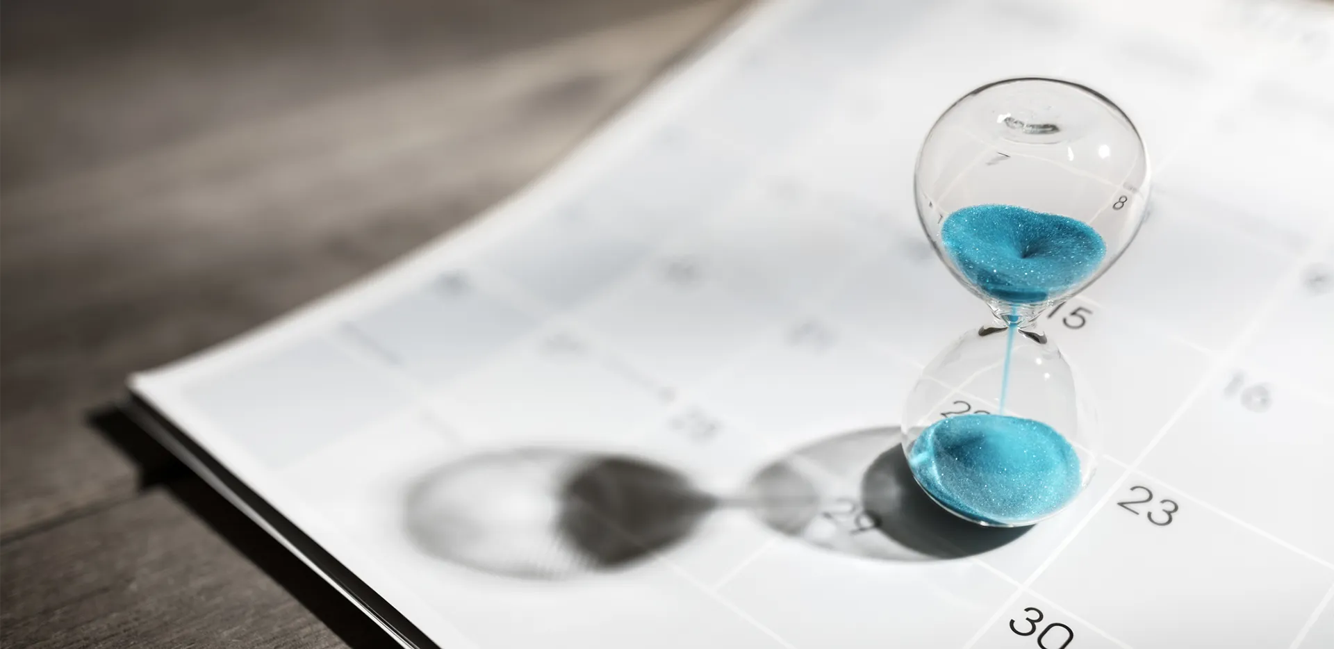 An hourglass with blue sand balanced on a calendar.