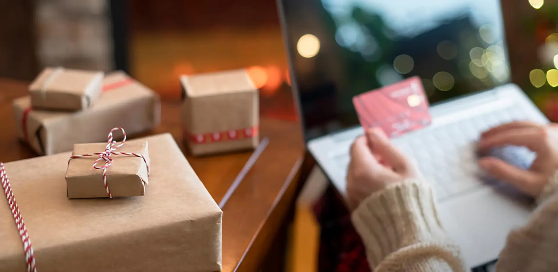 Someone shopping on their computer with a credit card with wrapped gifts next to them.