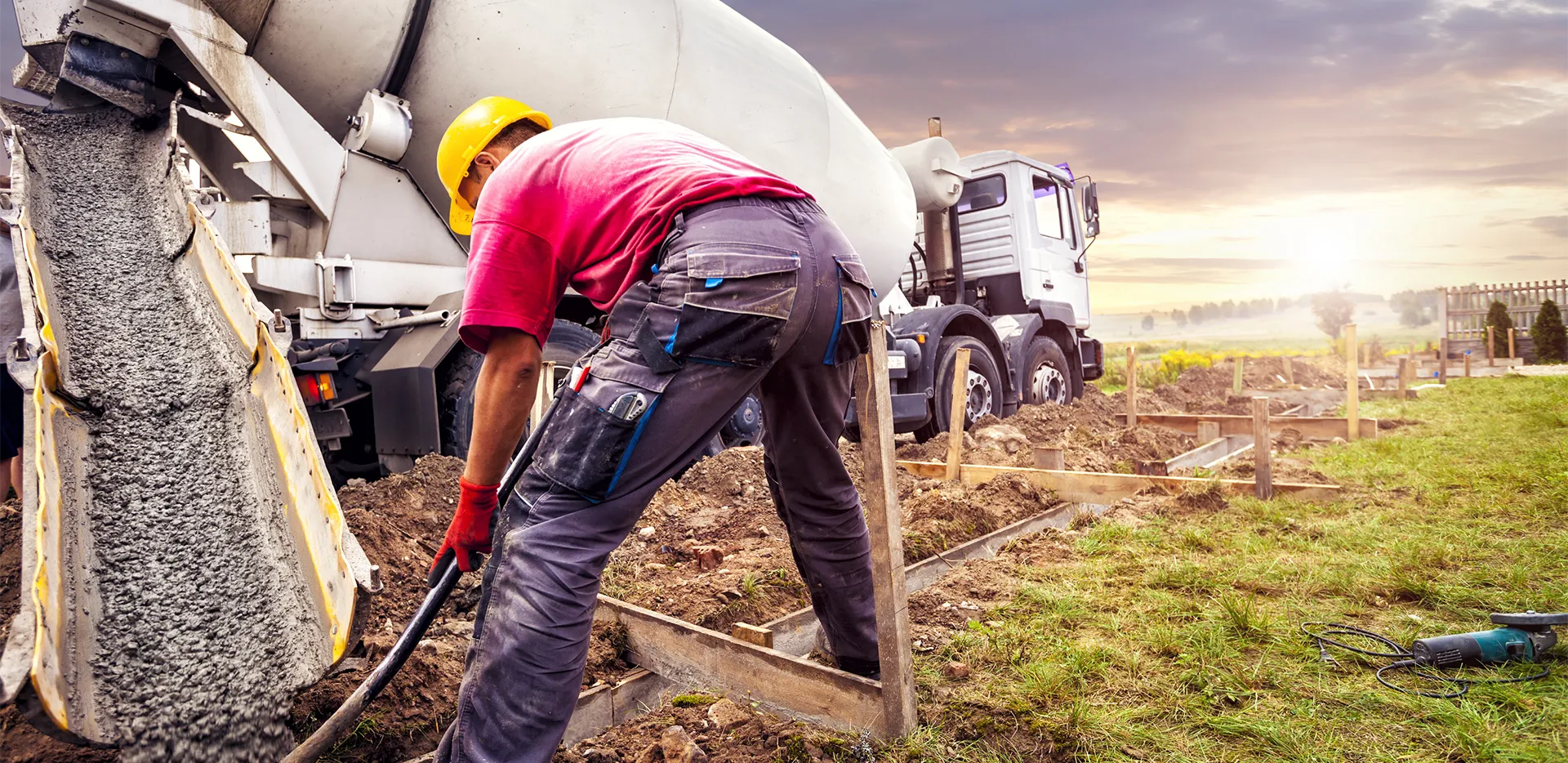 A contractor digging as a concrete truck pours out concrete.