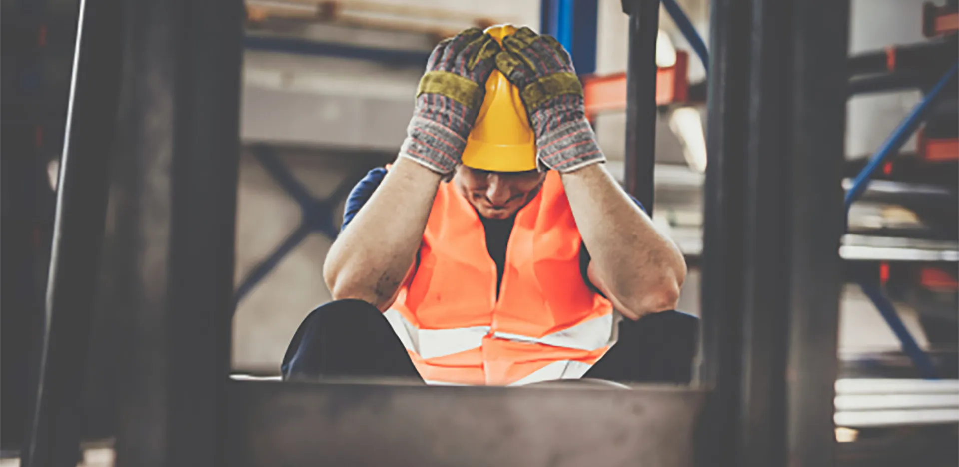 A construction worker wearing a hard hat sitting and clutching their head in frustration.